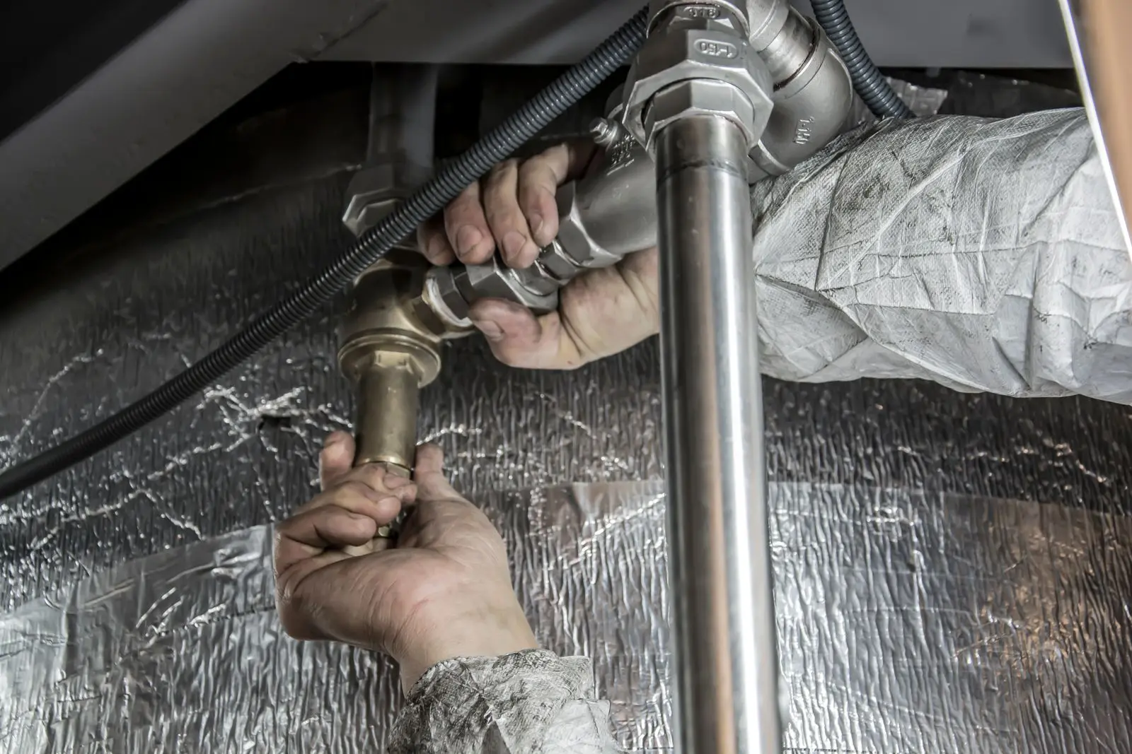 A Coastal Plumbing technician tightening pipe fittings under a sink