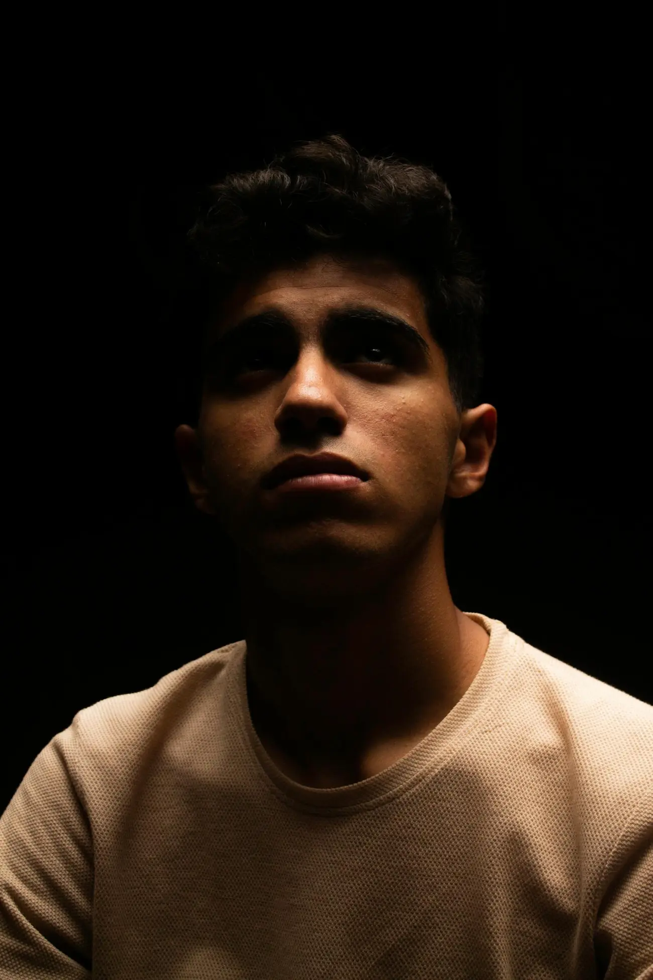 A moody, low-key studio portrait lit against a deep black background